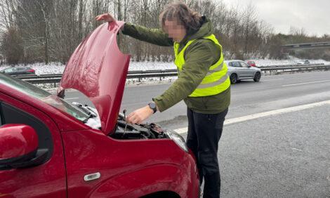 Die Front eines Fiat Panda ist von der Beifahrerseite aus zu sehen. Die Motorhaube wird gerade von einem jungen Mann mit einer Warnweste über einer Winterjacke geöffnet. Der Wagen steht auf dem Standstreifen einer zweispurigen Autobahn.