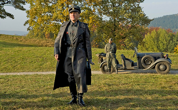 Christoph Waltz as the fictional SS officer Hans Landa in Inglourious Basterds. The main feature of his appearance is the long dark leather coat he is wearing on top of his grey SS uniform.