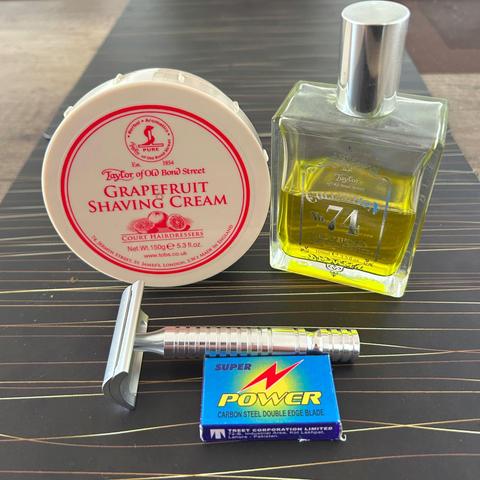 Das Bild zeigt eine Nahaufnahme verschiedener Herrenpflegeprodukte auf einem dunklen Untergrund. Zu sehen sind eine Dose Rasiercreme von Taylor of Old Bond Street mit Grapefruitduft, eine Flasche Aftershave namens No. 74 Victorian Lime Fragrance von Taylor of Old Bond Street, ein Rasierhobel und eine Packung Super Power Rasierklingen 