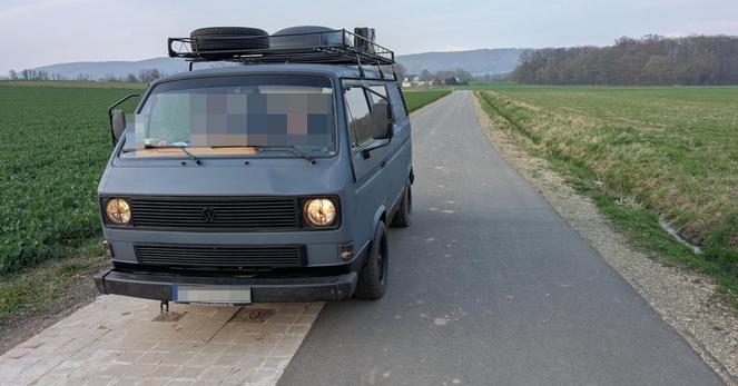Ein VW Bulli mit Reserverad und Ersatzbezinkanister auf dem Dachgepäckträger auf einer als Geh- und Radweg ausgeschilderten Straße.