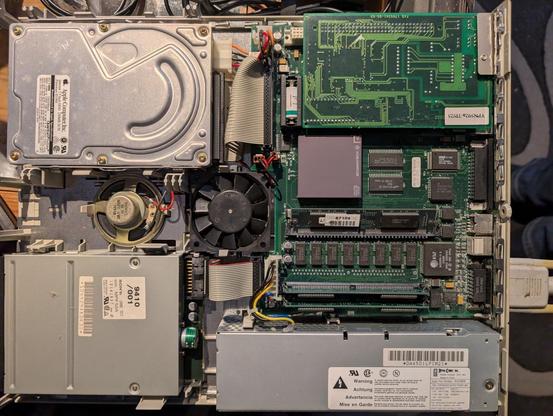 Das Innenleben eines Computers. Man sieht von oben ein Diskettenlaufwerk, eien Festplatte, das Mainboard mit einem Lüfter und Rambausteinen, sowie einem Netzteil.
