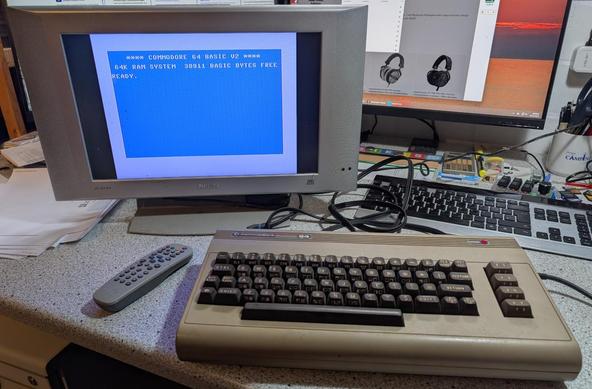 Ein Commodore C64 steht auf einem Schreibtisch. Ein alter 16:9-Flachbildfernseher zeigt den ikonischen Startbildschirm an.