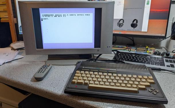 Ein Commodore plus/4 steht auf einem Schreibtisch. Ein alter 16:9-Flachbildfernseher zeigt den Startbildschirm an.