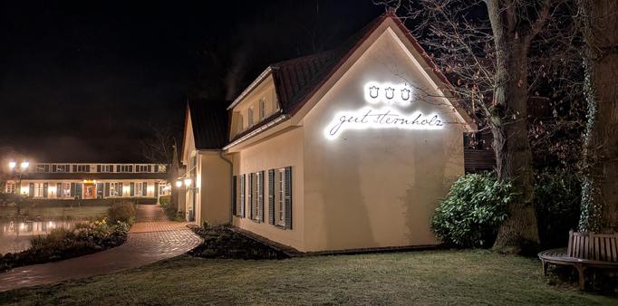 Ein im Dunklen fotografiertes Haus mit einem leuchtenden Schriftzug "Gut Sternholz" an der Stirnseite.