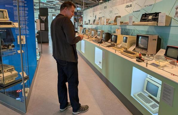 Ein Mann steht vor einer langen Galerie alter Computer, welche auf einem thekenähnlichen, langen Sideboard ausgestellt sind.