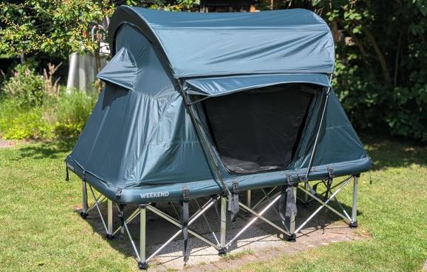 Ein aufgebautes, grünes Dachzelt "Groenberg Weekend Comfort" steht auf der "Groenberg Weekend Stage". Einem ausfaltbaren Ständer für ein Dachzelt, damit dieses nicht direkt auf dem Boden steht.