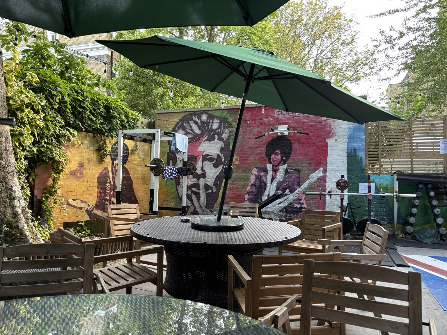 Hof mit rundem Tisch und Holzstühlen, Sonnenschirm, Fitnessgeräten und Graffiti an der Wand