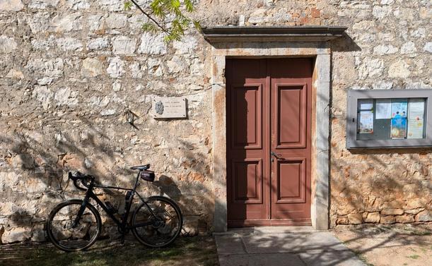 Ein Fahrrad lehnt an einer Hauswand aus Natursteinen neben einer Alten Holztür.