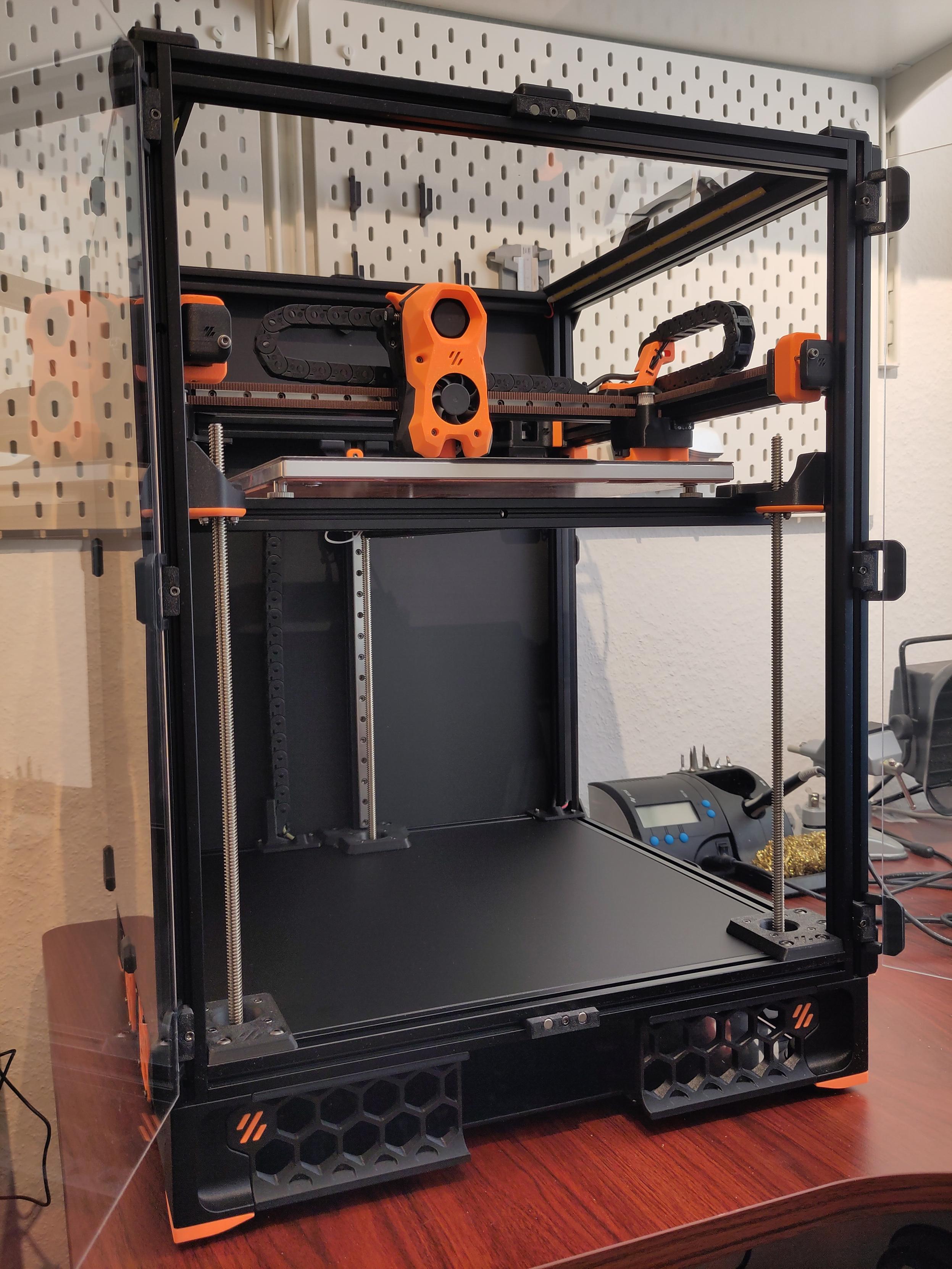 A mostly finished Voron Trident 3D printer. The protective film has been removed from the panels and doors. Only the Touchscreen at the bottom center is missing.