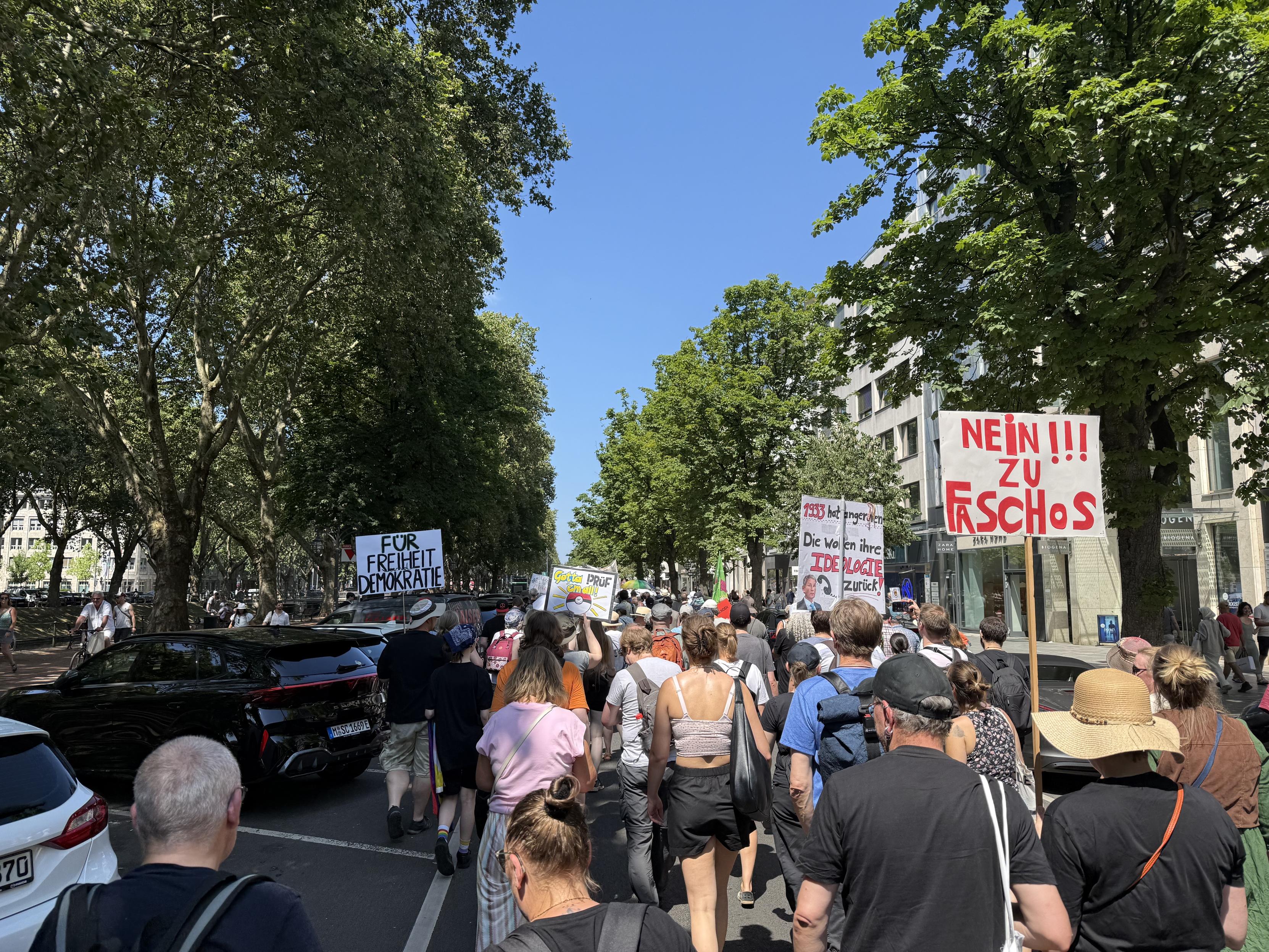 Unsere Prüfdemo füllt die Kö. Über uns der strahlend blaue Himmel – völlig wolkenfrei. Die Schilder mit »Nein zu Faschos!!!« oder »1933 hat angerufen – Die wollen ihre Ideologie zurück!« (mit einem Bild von Benjamin Höcke 🙈😹) oder »Gotta prüf em all« drücken deutlich die Wünsche der Teilnehmenden aus …