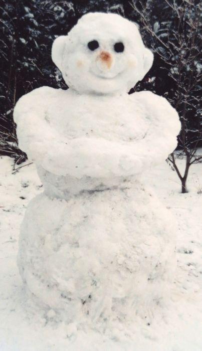 eine Schneefigur aus dem üblichen drei Schneekugeln in verschiedenen Größen vor einem dunklen Hintergrund. Er/Sie hat die Arme vor der Brust verschränkt, das Gesicht hat große runde schwarze Augen eine rote Knubbelnase, einen lächelnden roten Mund, rechts und links sind große Löffelohren.