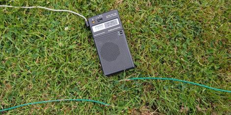 Ein kleines Grundig-Taschenradio liegt auf einer Rasenfläche. Darunter sieht man eine Begrenzungsschnur für einen Rasenmäherroboter, die offensichtlich durchtrennt wurde.