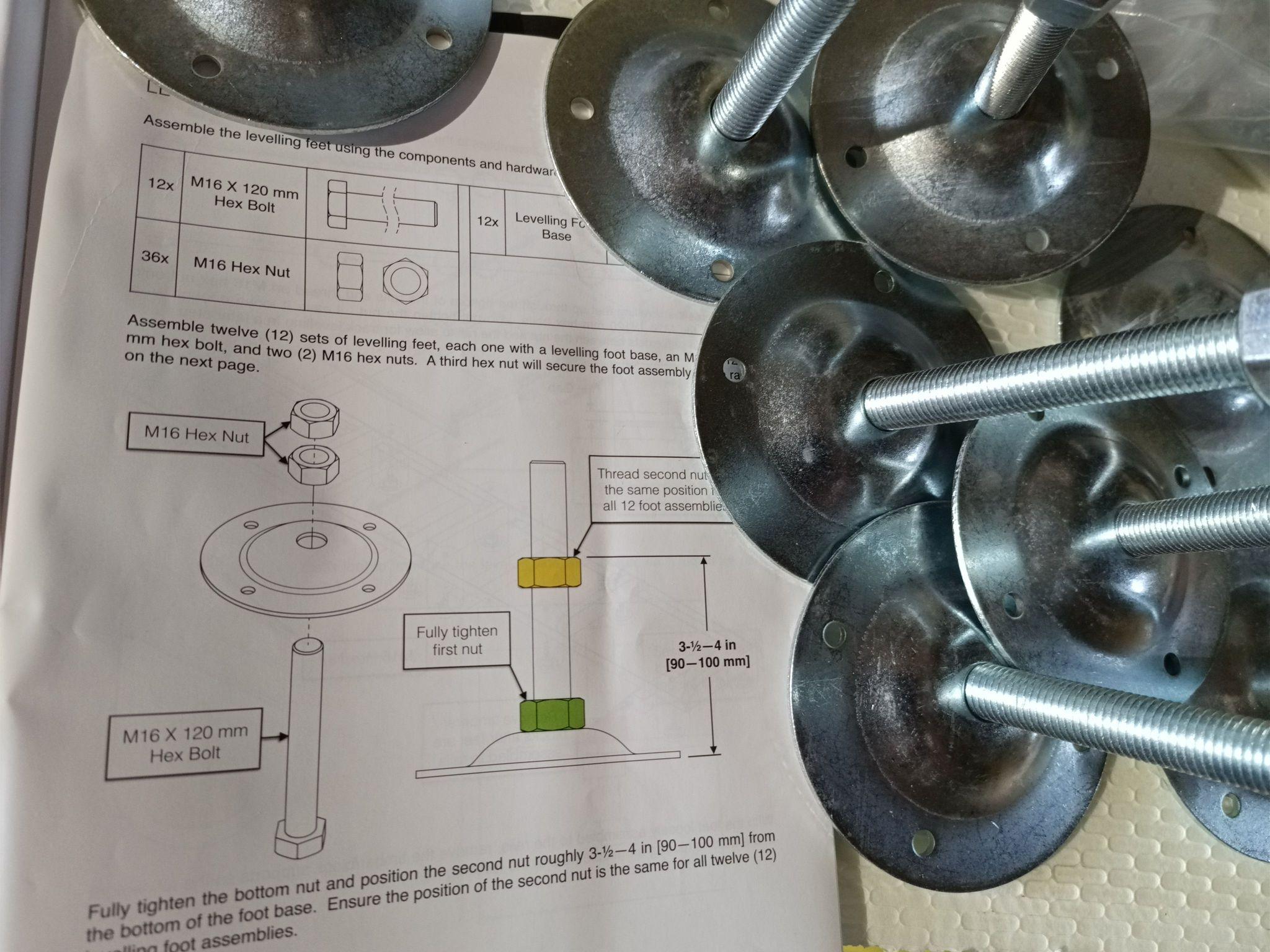 Steel feet being assembled with long adjustable bolts and wide, circular steel plate bottoms. They're on top of a manual describing how to put them together.