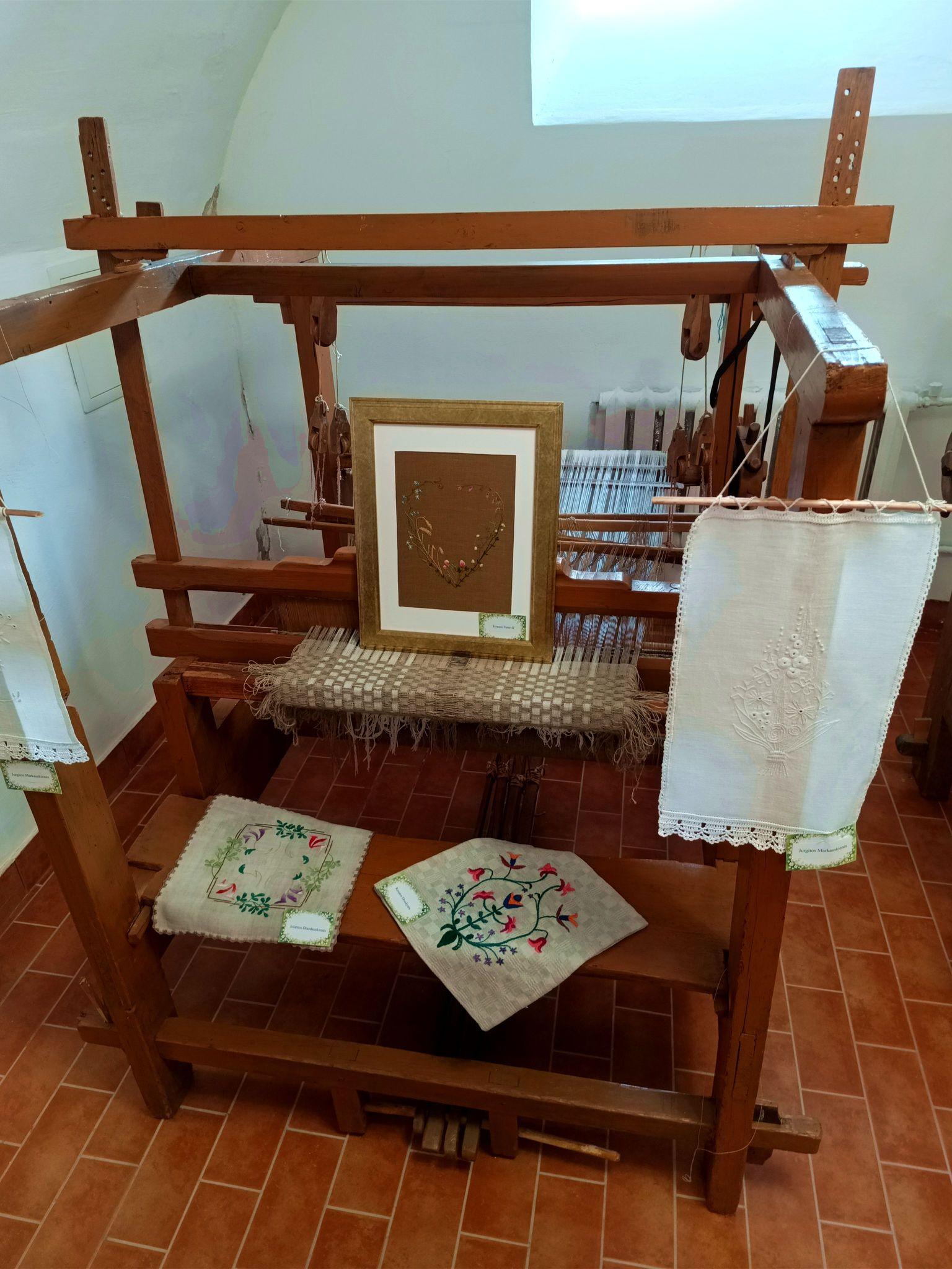 A wooden loom with some woven and stitched fabric exhibits on it.