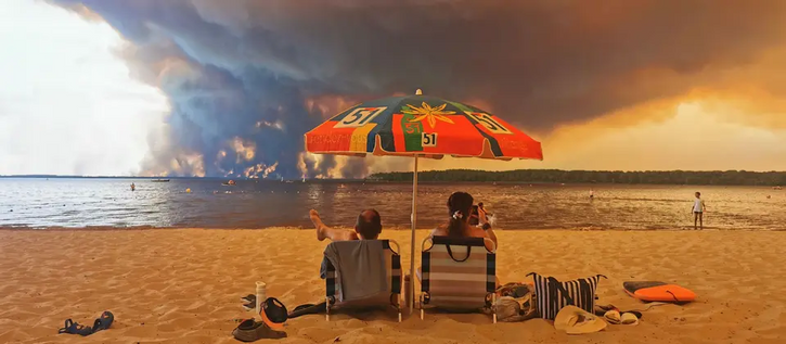 Kopiertes Titelbild vom verlinkten Tagesschau-Beitrag. Inhalt:

Vordergrund zwei Menschen in gemütlicher Pose in Liegestühlen an einem Strand, fotografiert von hinten, dazwischen ein Sonnenschirm.

Mittelgrund: eine große Wasserfläche, fast ohne Wellen, einzelne badende Menschen.

Hintergrund: ein dunkler Waldstreifen am anderen Ufer (der Bucht oder des Sees), ca. ein Viertel davon steht in Flammen und verursacht dunkelgraue Wolken die einen Großteil des ansonsten blau-grauen Himmels bedecken.
…