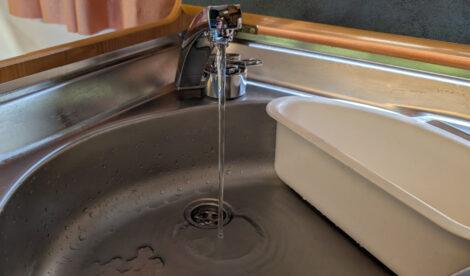 Aus einem verchromten Wasserhahn läuft Wasser in die Edelstahlspüle eines Wohnwagen