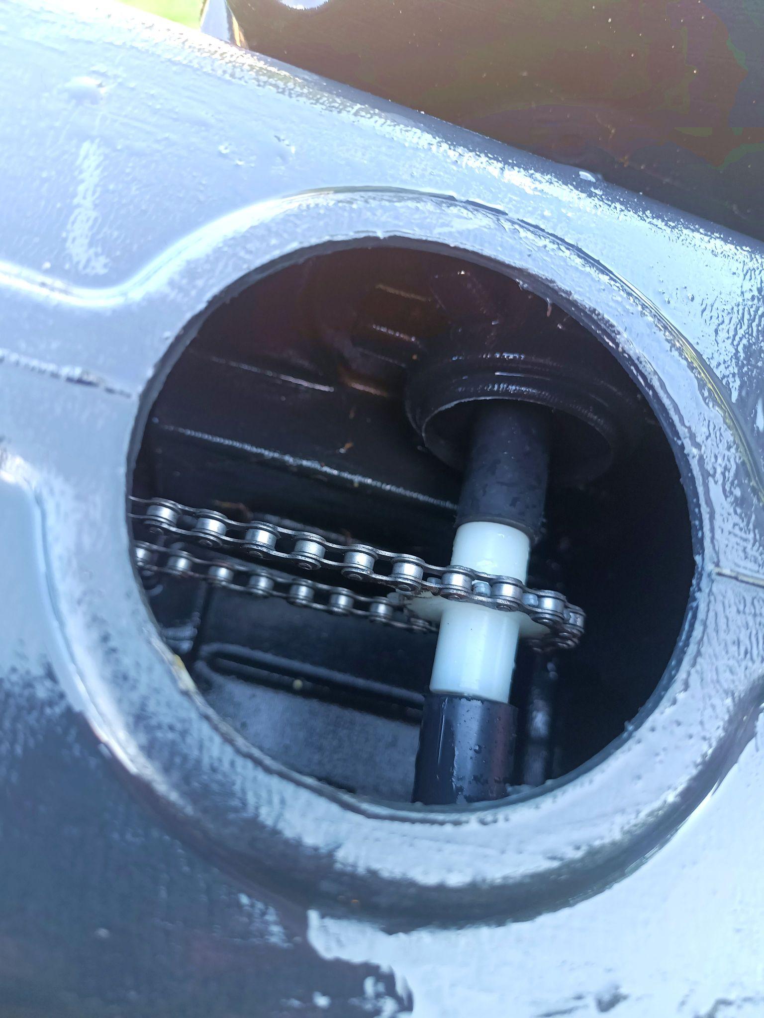 An access hole in the bottom with a drive chain on a plastic sprocket, now cleaned of sand.