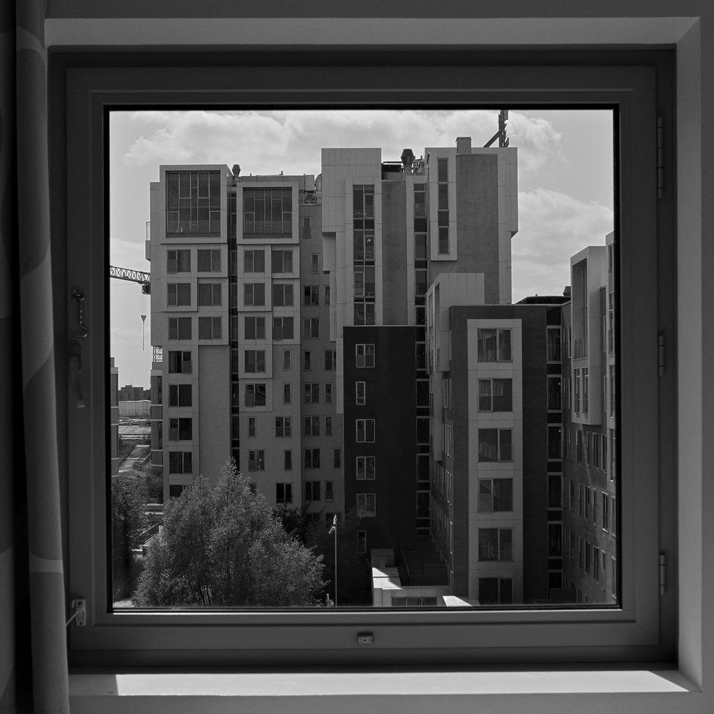 Blick durchs quadratische Fenster auf ein Hochhaus und den seitlichen Flügel des Hotelkomplax sowie angrenzende Häuser.