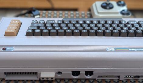 Die Rückansicht eine Commodore C64 Ultimate von schräg oben. Man sieht die hinteren Anschlussports und zwischen dem Expansionsport und dem RF bzw. Audioausgang einen kleinen beigen Kasten mit drei schwarzen Knöpfen.