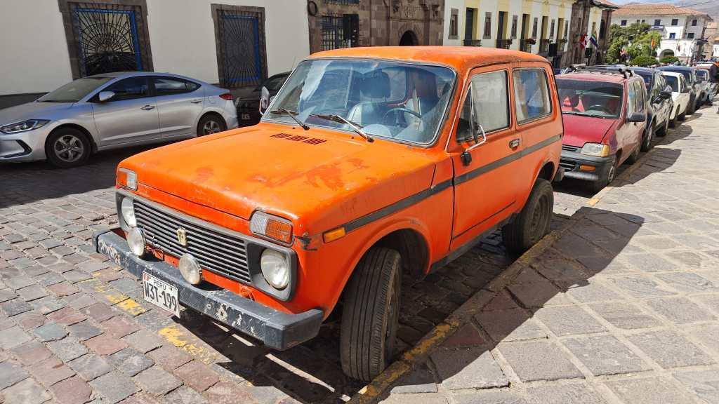 Orangefarbener Lada Niva parkt am Straßenrand.